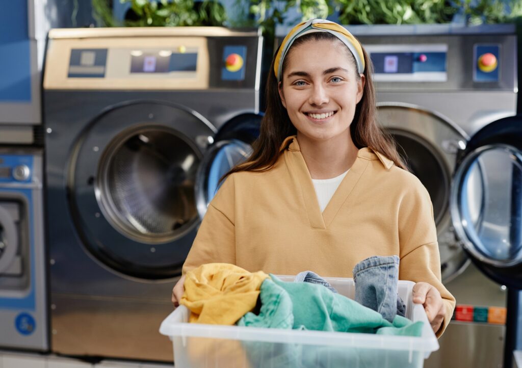 Pretty girl in casualwear holding plastic container with clean clothes
